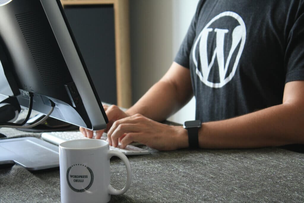 un homme avec un t-shirt noir et le symbole wordpress qui tape sur le clavier d'un ordinateur